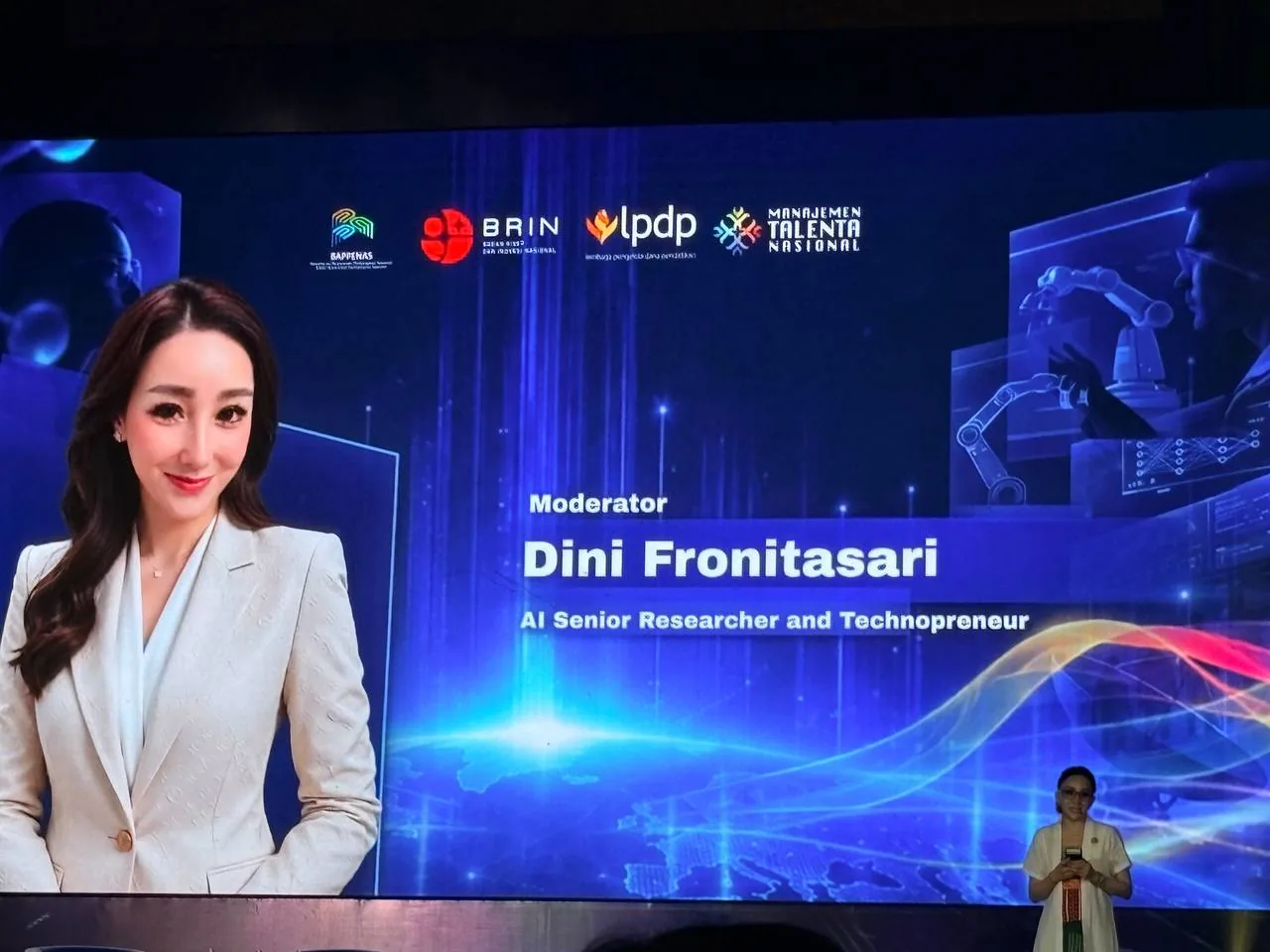 Layar panggung memperkenalkan moderator Dini Frontasari