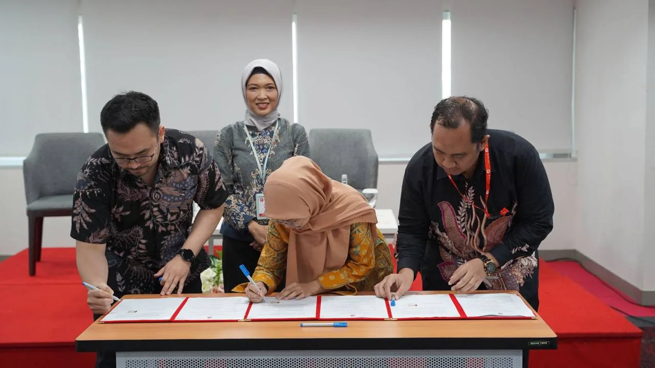 Tiga peserta menandatangani dokumen di meja dalam ruang acara resmi